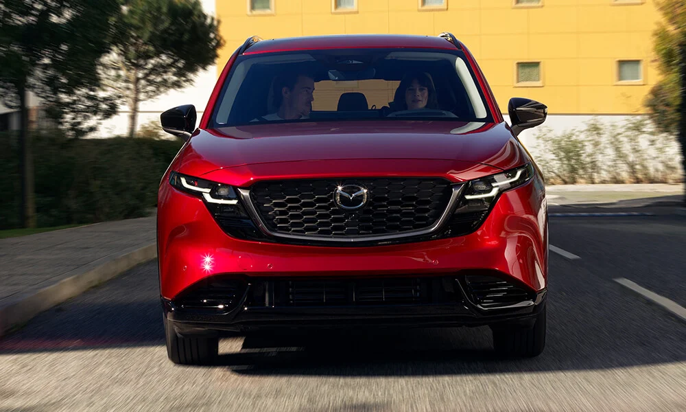 Vue d’un angle bas d’un Mazda CX-5 rouge vibrant cristal métallisé roulant sur une route.