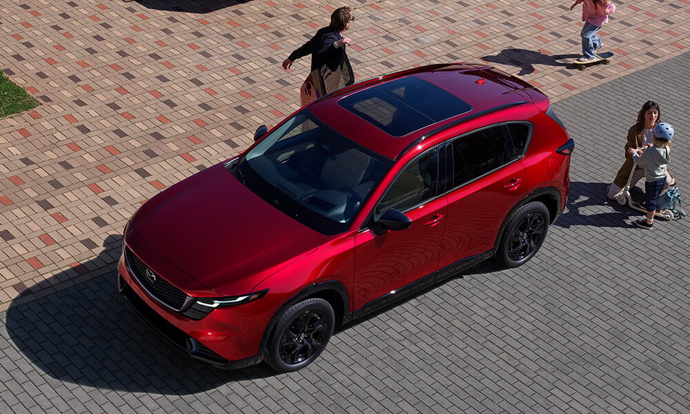 Vue de haut d’une famille se tenant autour d’un Mazda CX-5 avec des enfants qui jouent.