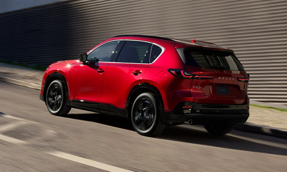 Soul Red Crystal Metallic Mazda CX-5 driving uphill, shown from the driver’s side rear with a motion-blurred background. 